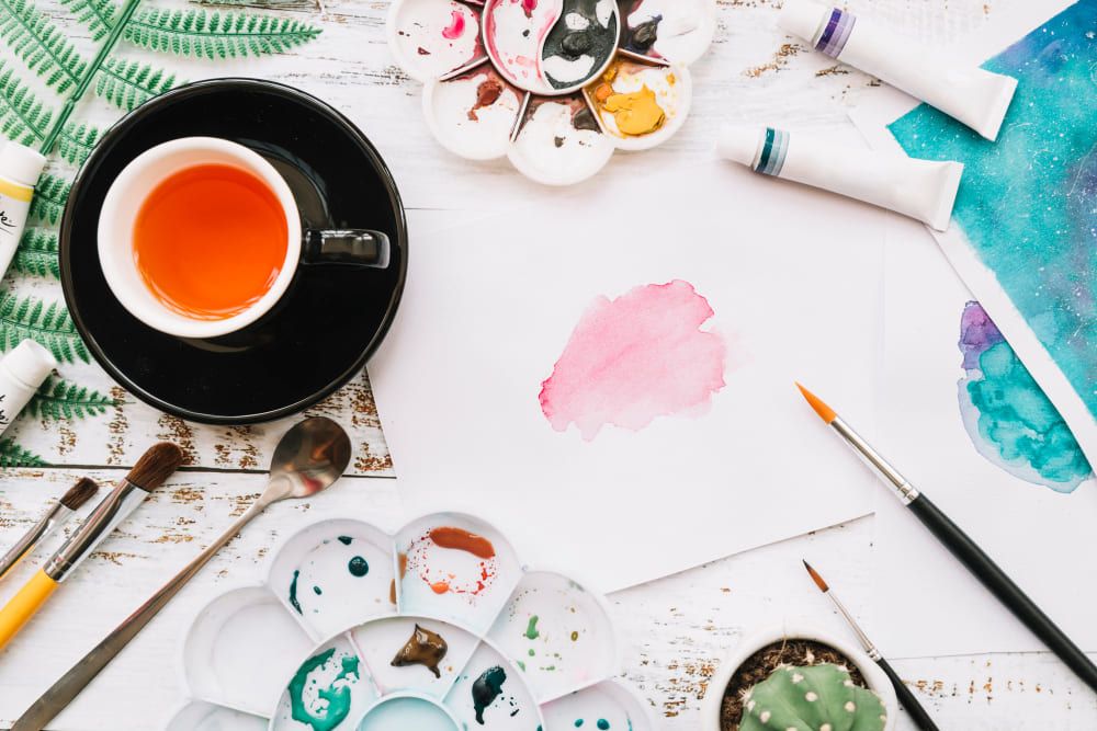 une tasse de thé avec des feuilles, des pinceaux et des aquarelles 