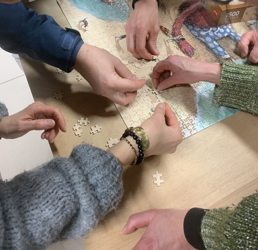 La photo représente des mains qui assemblent des pièces de puzzle ensemble